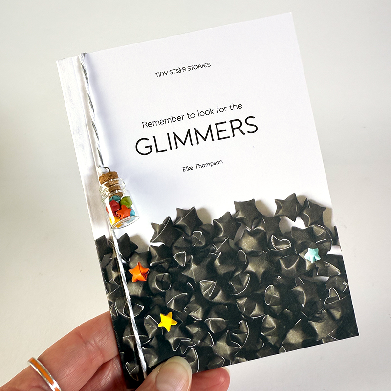 A hand holding the A6 sized book Remember to look for the GLIMMERS – A Tiny Star Stories book